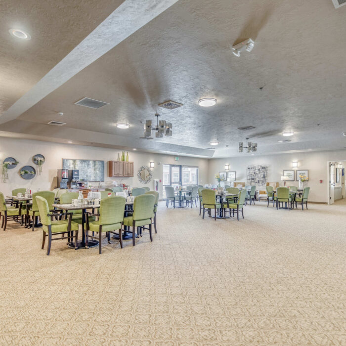Large open assisted living dining hall with green chairs and round tables for group meals.